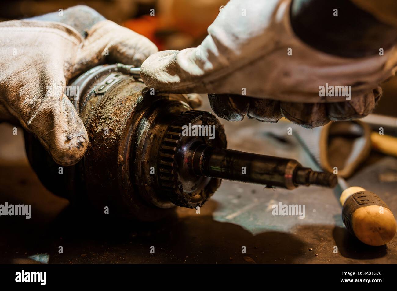 Nahaufnahme der Hände eines Mechanikers mit Schutzhandschuhen, die ein altes, fettiges Kfz-Teil mit Werkzeugen reparieren. Stockfoto