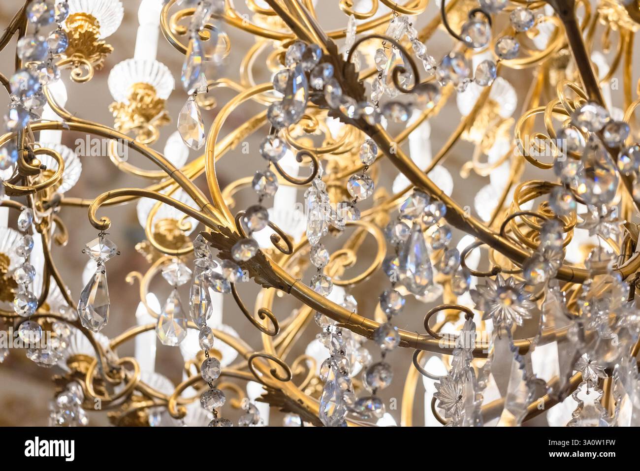Goldener Kristalllüster, der unter hellen Lichtern glitzert, mit komplizierten Metallarbeiten und eleganten Designdetails, perfekt für luxuriöse Orte Stockfoto