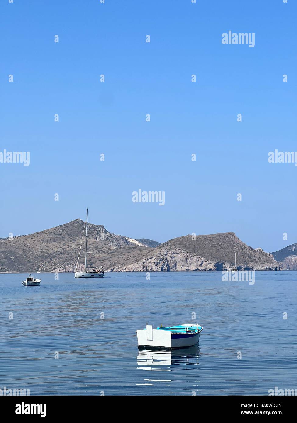 Ein weißes und blaues Boot treibt auf stillen Gewässern, mit Inseln dahinter - Smartphone-aufgenommenes Stockfoto