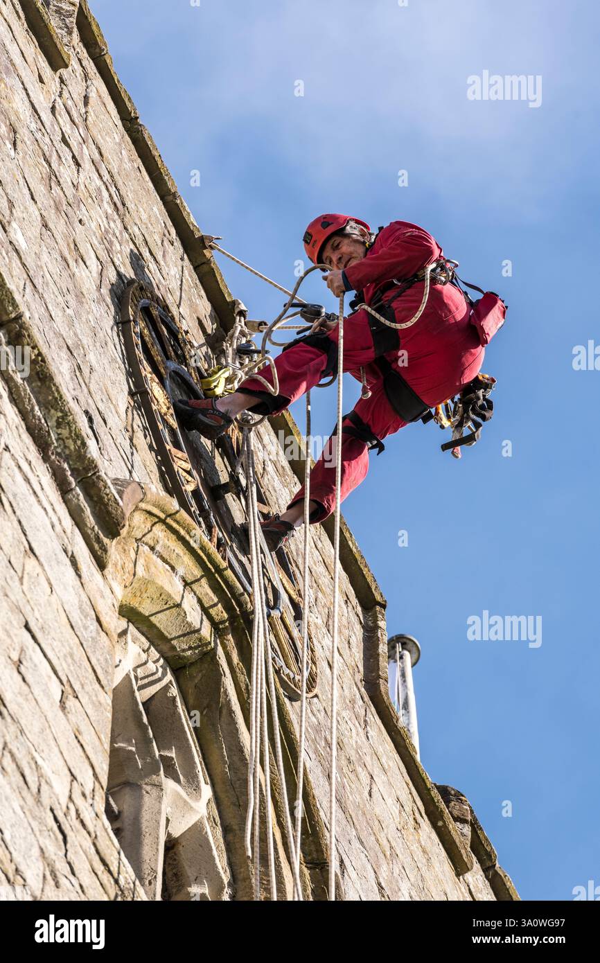 Der 77 Jahre alte Turmjäger Chris Milford hoch auf dem mittelalterlichen Turm der St. Andrew's Church, Presteigne, Powys, entfernt die alte 19c-Uhr für Renovierung und Regilding (Wales, Großbritannien). Chris arbeitet für WallWalkers Ltd. Aus Bristol Stockfoto