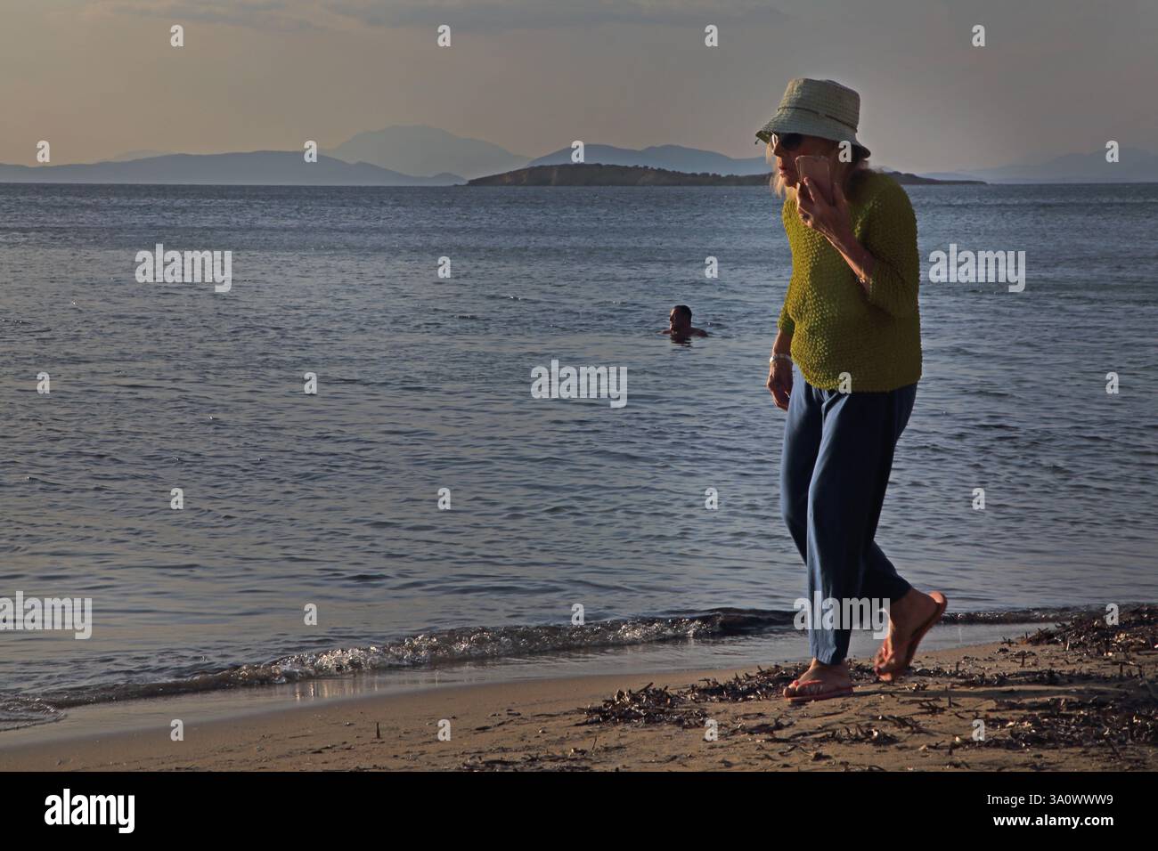Frau, die entlang der Küste mit Handy Vouliagmeni Beach Athen Attika Griechenland läuft Stockfoto