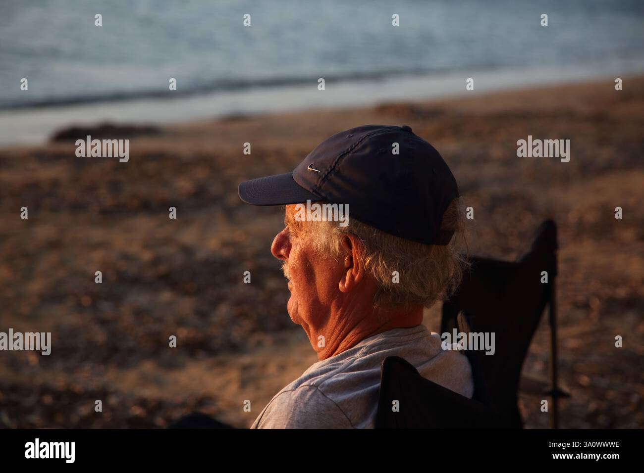 Mann sitzt am Strand von Vouliagmeni und beobachtet den Sonnenuntergang am Meer Athen Attika Griechenland Stockfoto