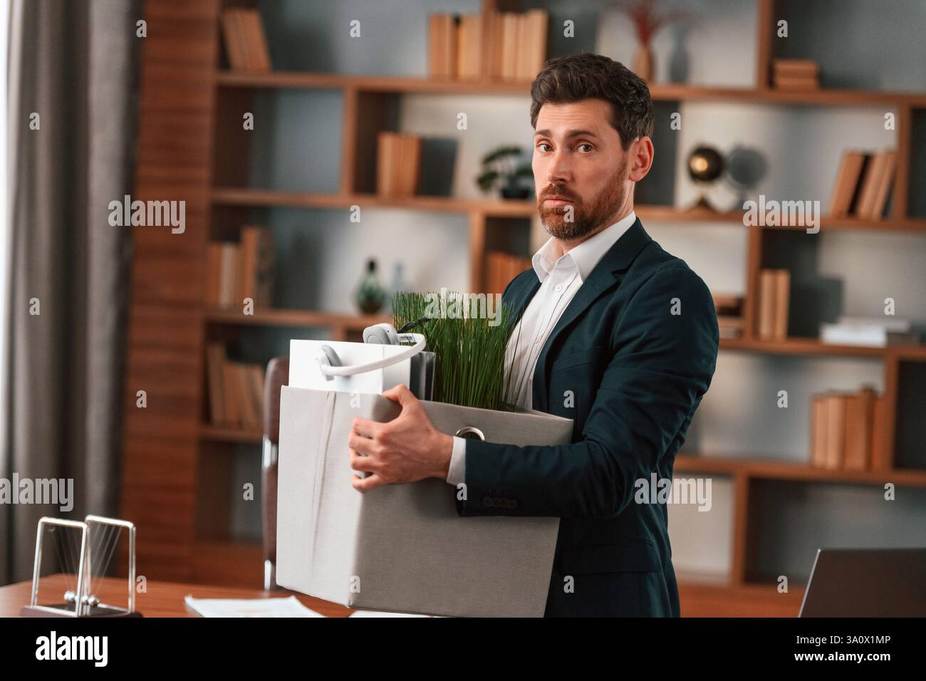 Mit einer Schachtel Zeug drin. Geschäftsmann in formeller Kleidung arbeitet drinnen. Stockfoto
