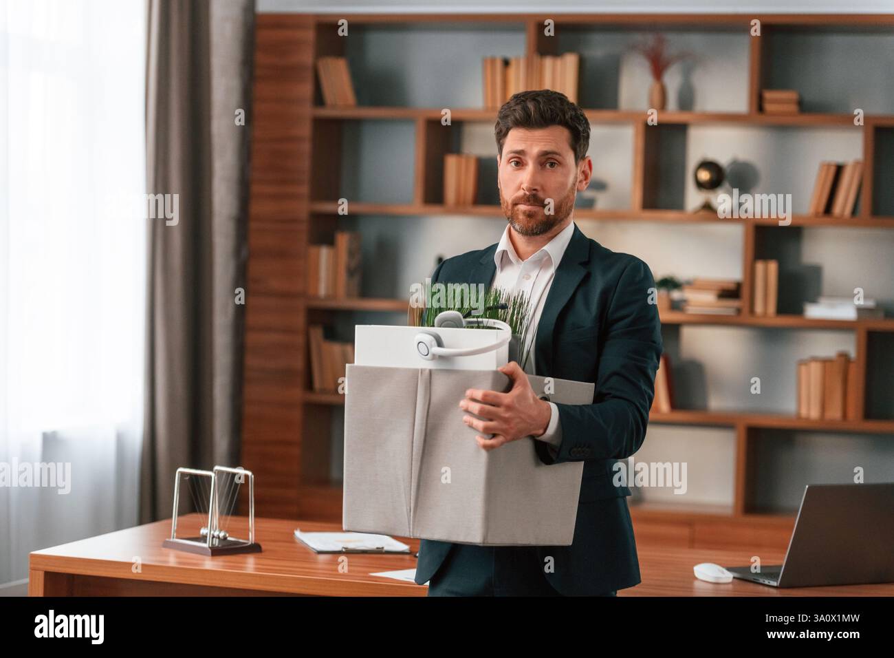 Mit einer Schachtel Zeug drin. Geschäftsmann in formeller Kleidung arbeitet drinnen. Stockfoto