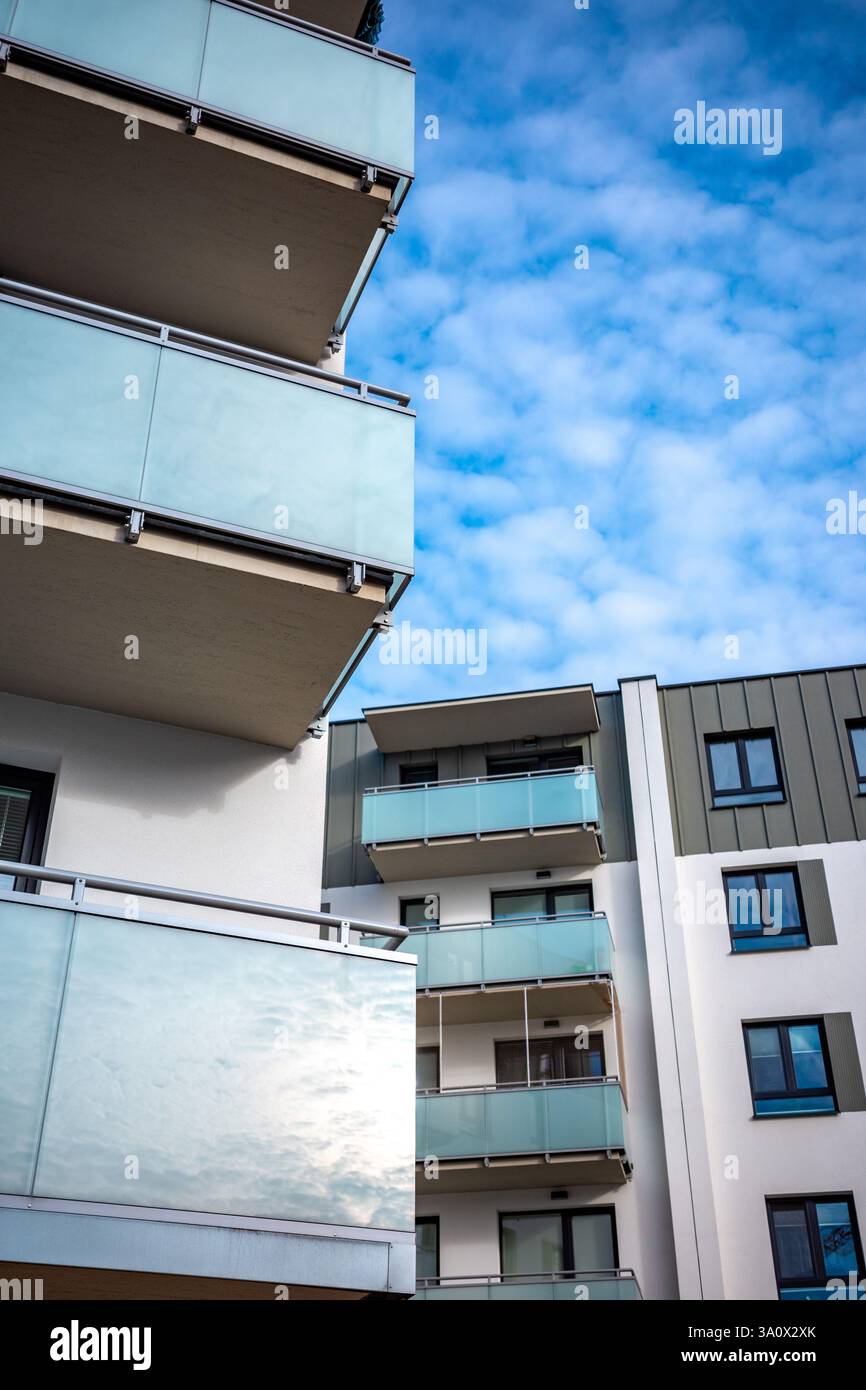 Die hellgraue Fassade eines modernen Apartmenthauses vor dem blauen Himmel. Die Apartments sind mit verglasten Balkonen ausgestattet. Stockfoto