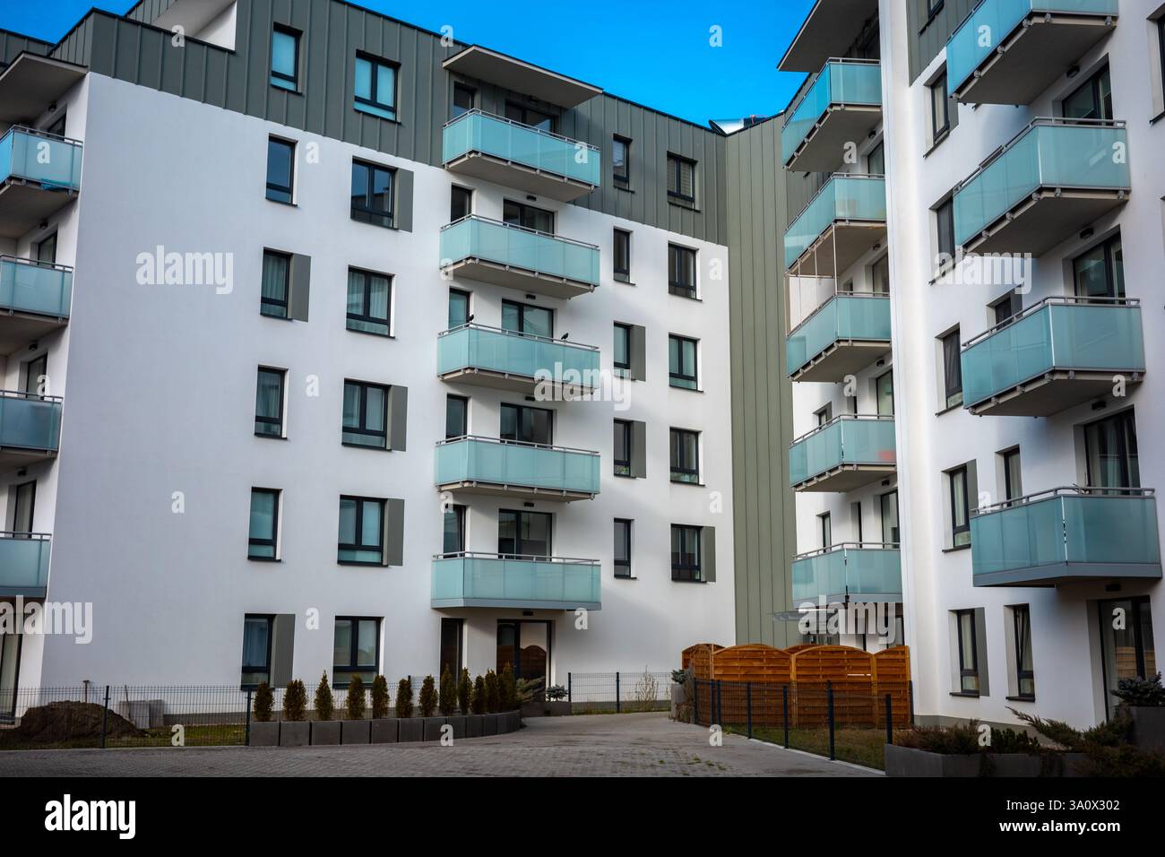 Die hellgraue Fassade eines modernen Apartmenthauses vor dem blauen Himmel. Die Apartments sind mit verglasten Balkonen ausgestattet. Stockfoto