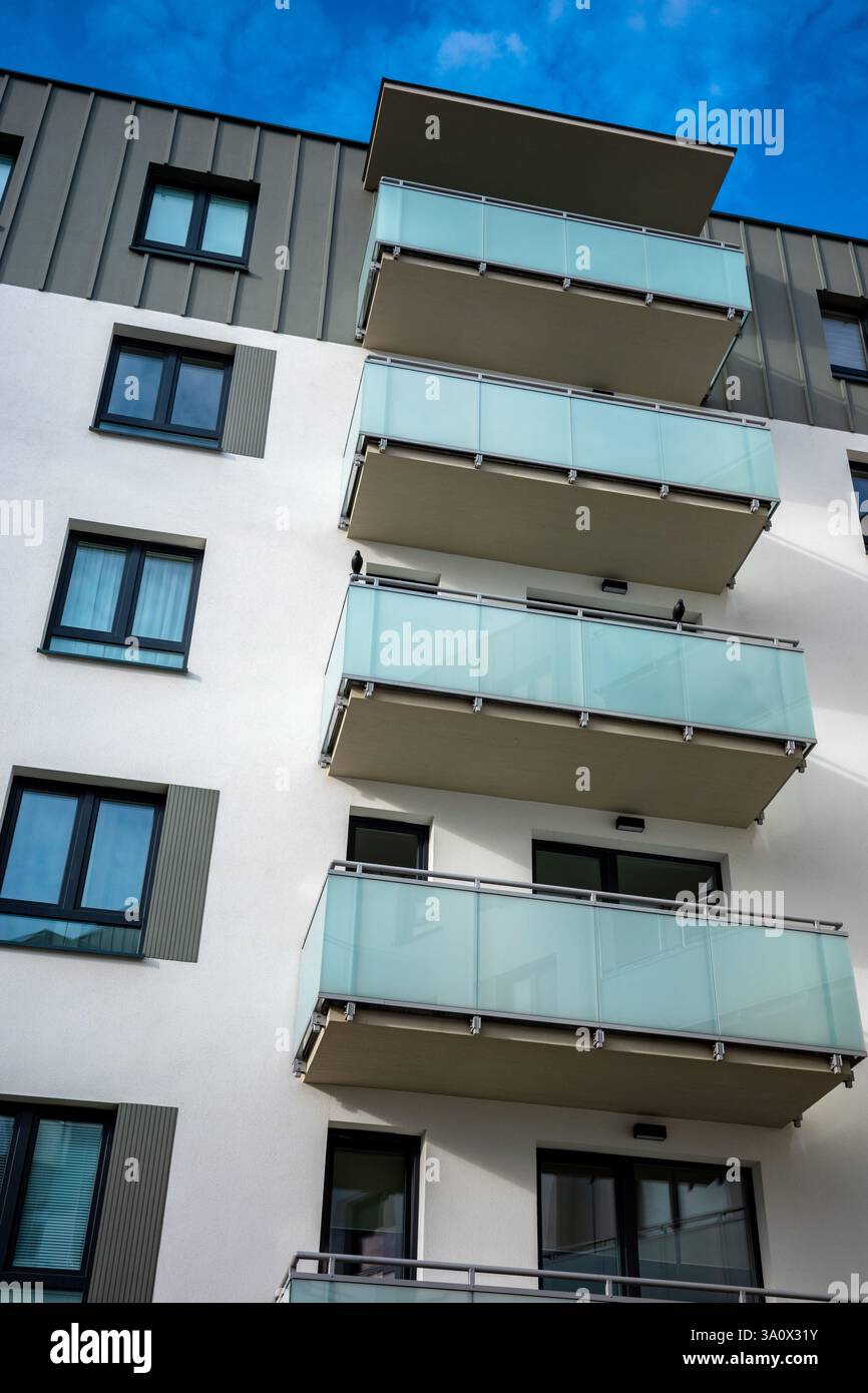 Die hellgraue Fassade eines modernen Apartmenthauses vor dem blauen Himmel. Die Apartments sind mit verglasten Balkonen ausgestattet. Stockfoto
