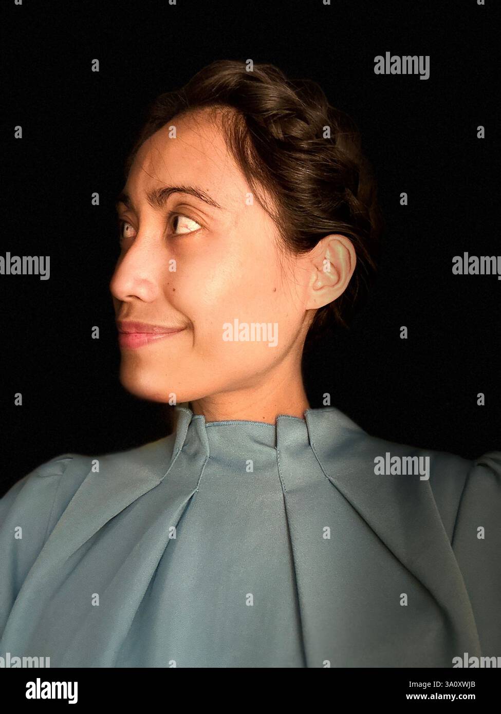 Porträt einer Frau mit geflochtenen Haaren, die ein lässiges Kleid vor schwarzem Hintergrund trägt. Stockfoto