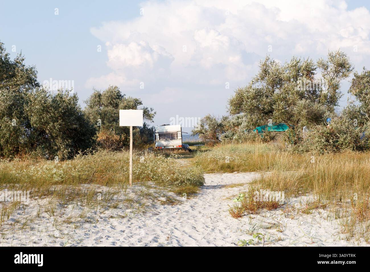Ein Wohnwagen parkt in der Nähe eines Sandstrandes, umgeben von wilder Vegetation und Bäumen, was einen ruhigen und abgeschiedenen Campingplatz schafft. Stockfoto