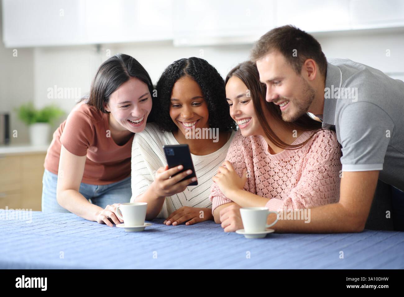 Glückliche interrassische Gruppe von Freunden, die zu Hause in der Küche telefonieren Stockfoto