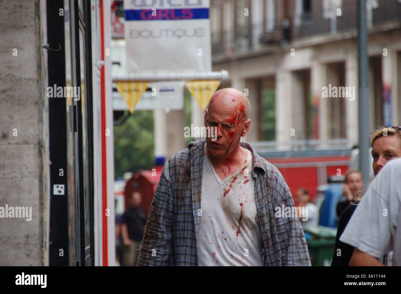 Bruce Willis als John McClane, bedeckt mit Kunstblut, am die Hard 5-Set in Budapest. Ein Feuerwehrauto und eine Crew sind bei diesem Action-Szene-Shooting zu sehen Stockfoto