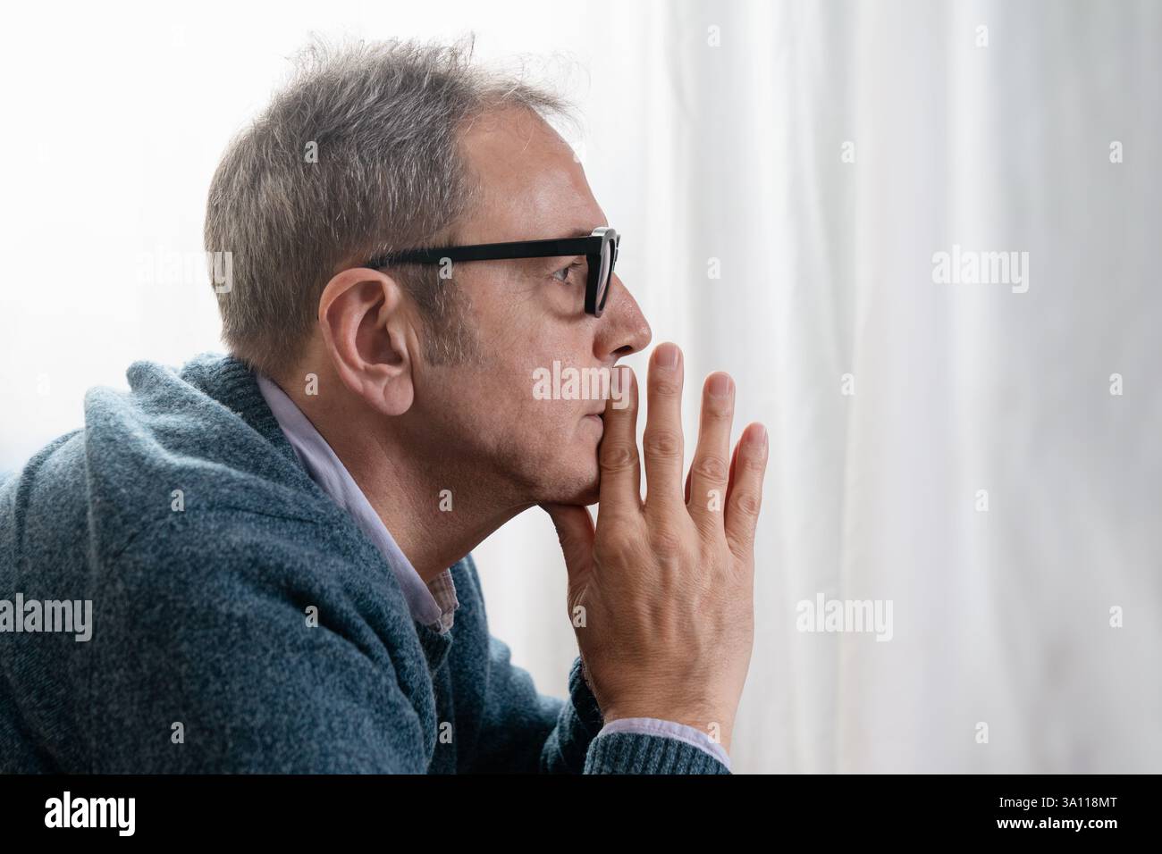 Nahaufnahme eines älteren Mannes in tiefem Denken, seine Hand auf seinem Kinn, mit einem ernsten und kontemplativen Ausdruck wegblickend. Entscheidungskonzept- Stockfoto