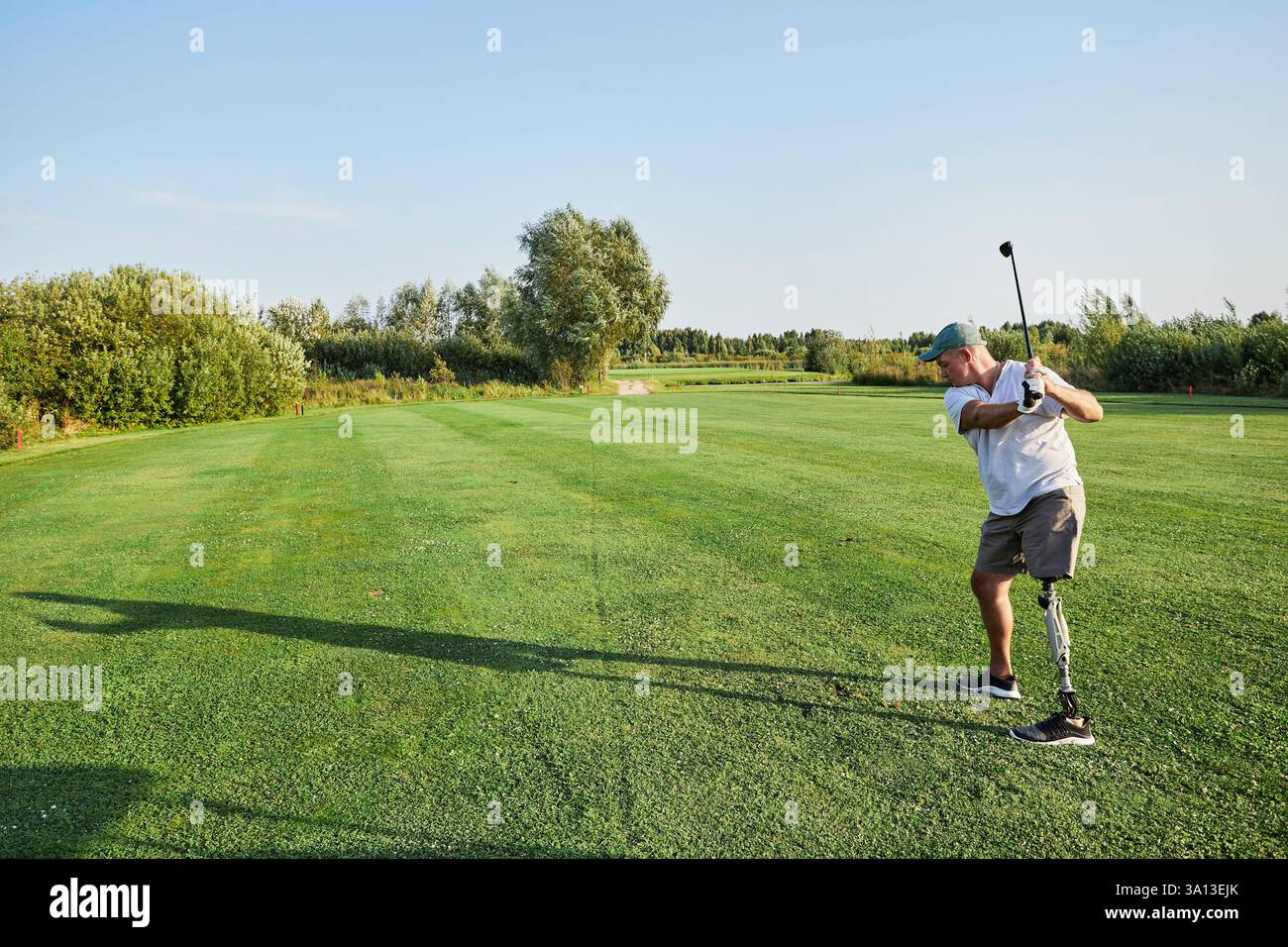 Ein Golfer mit einer Beinprothese schwingt an einem Sommernachmittag souverän auf einem grünen Fairway unter klarem blauem Himmel. Stockfoto