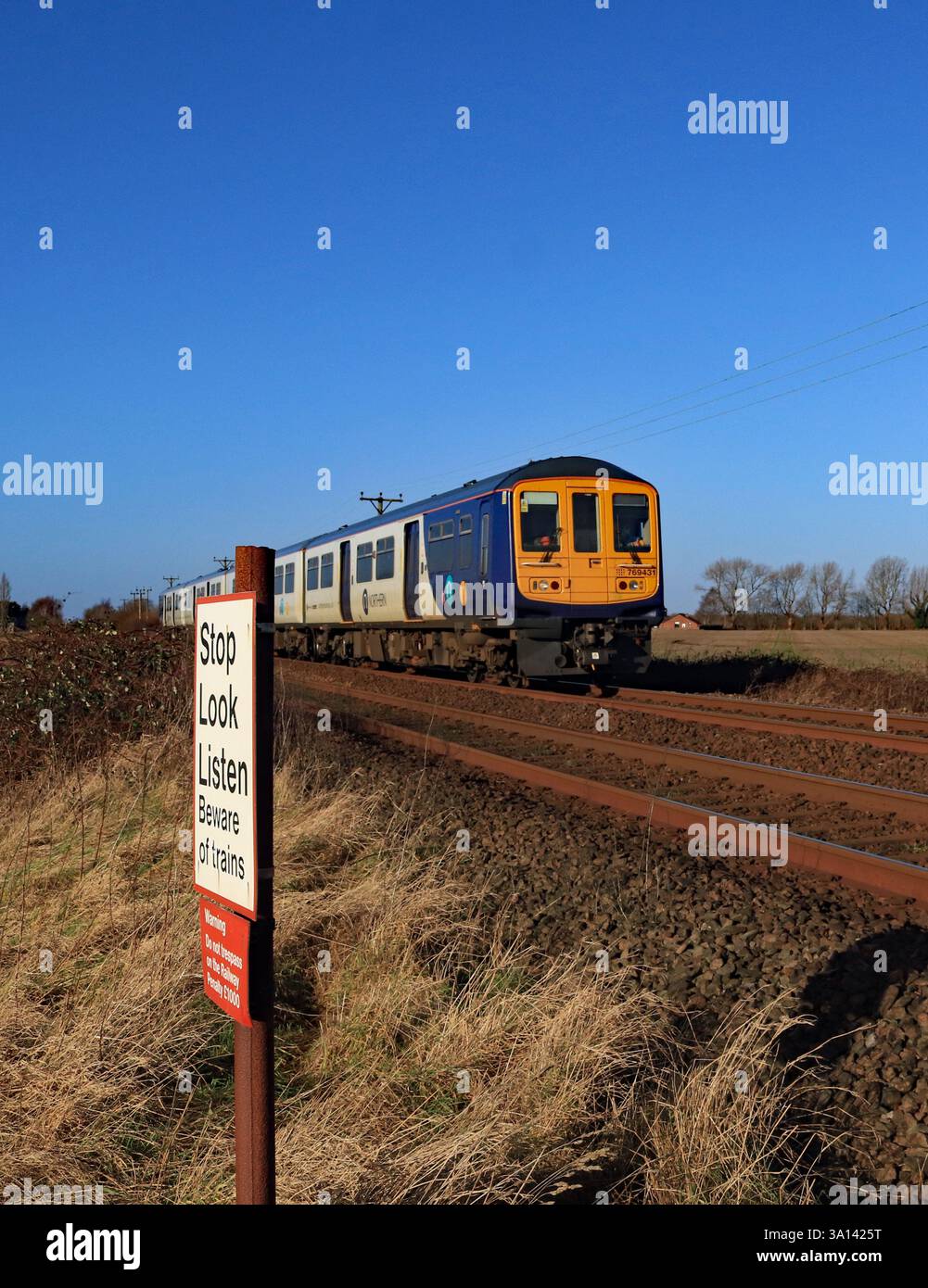 Unter dem breiten blauen Himmel von West Lancashire nähert sich ein Zug der Northern Railway auf der Strecke von Southport nach Wigan Stockfoto