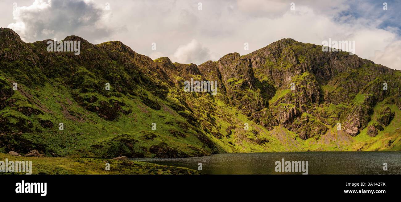 Dramatische Berglandschaft von Llyn Cau und Cadair Idris, Snowdonia – zerklüftete Gipfel, üppige grüne Hänge und ruhiger Gletschersee unter stürmischem Himmel Stockfoto