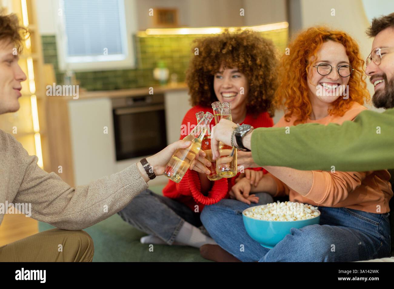 Freunde treffen sich in einem stilvollen Wohnzimmer und heben Gläser mit erfrischenden Getränken auf. Sie teilen Lachen und Wärme, während sie von einer Schüssel p umgeben sind Stockfoto