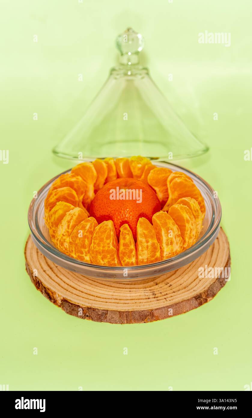 Eine leuchtende Mandarinenkrone aus segmentierten Scheiben auf rustikalem Holz und mit einer Glasglocke gekrönt, die die lebendige Kunst der Zitrusfrüchte in minimalem Maße zelebriert Stockfoto