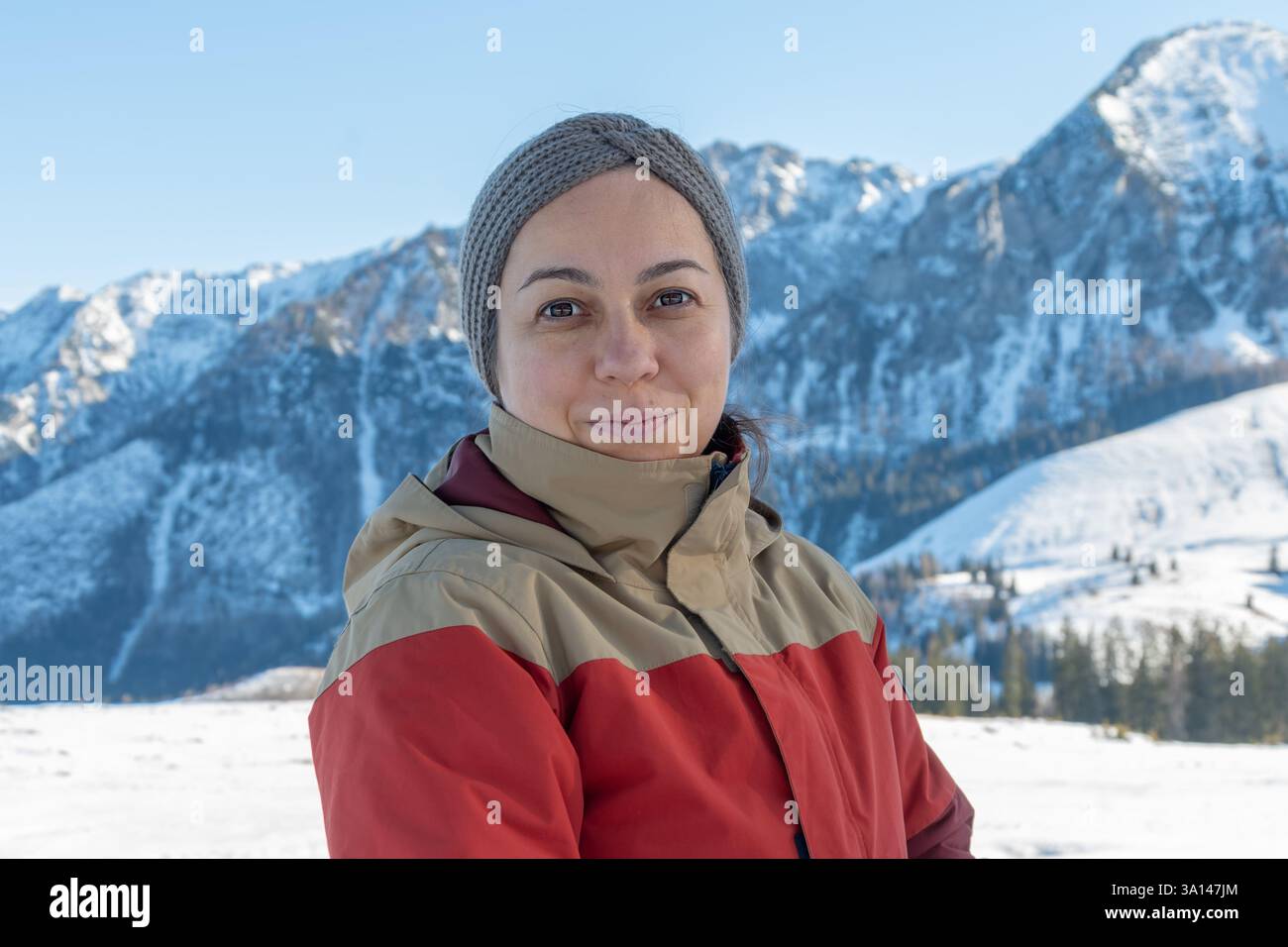 Porträt einer 45-50-jährigen Frau in einer warmen Jacke, die die frische Bergluft genießt und sich vor dem Hintergrund verschneite Berghänge posiert Stockfoto