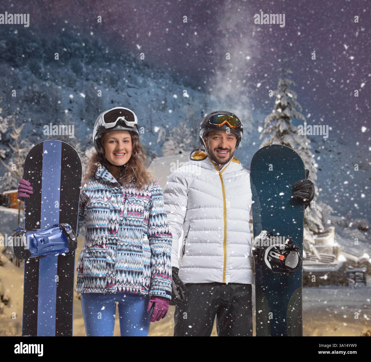 Junger Mann und Frau mit Snowboards in einer verschneiten Nacht am Berg Stockfoto