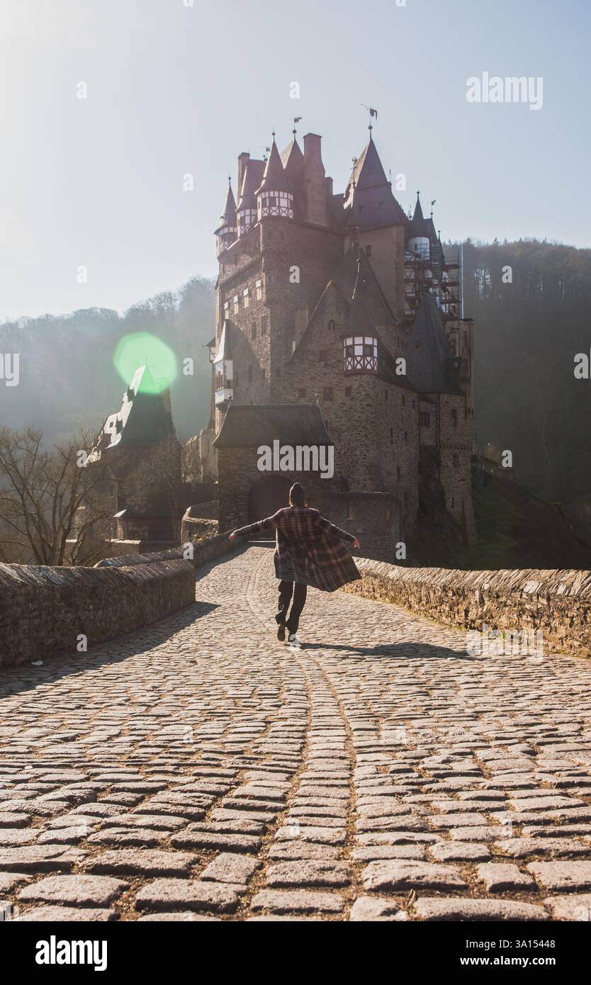 Frau rennt in ihrem modischen Winter-Herbstoutfit auf eines der schönsten Schloss der Welt, Schloss Eltz in Deutschland. Reisekonzept Stockfoto