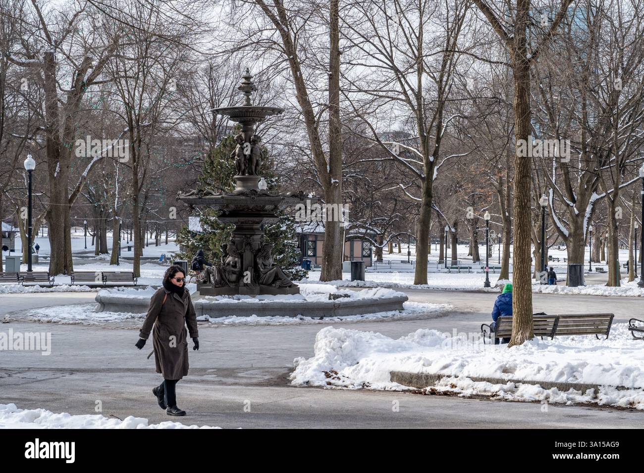 Boston, MA, USA - 11. Februar 2025 - Eine Frau im Wintermantel Walking Pass Brewer Fountain in Boston Common an einem Wintertag mit Schnee auf dem Boden Stockfoto