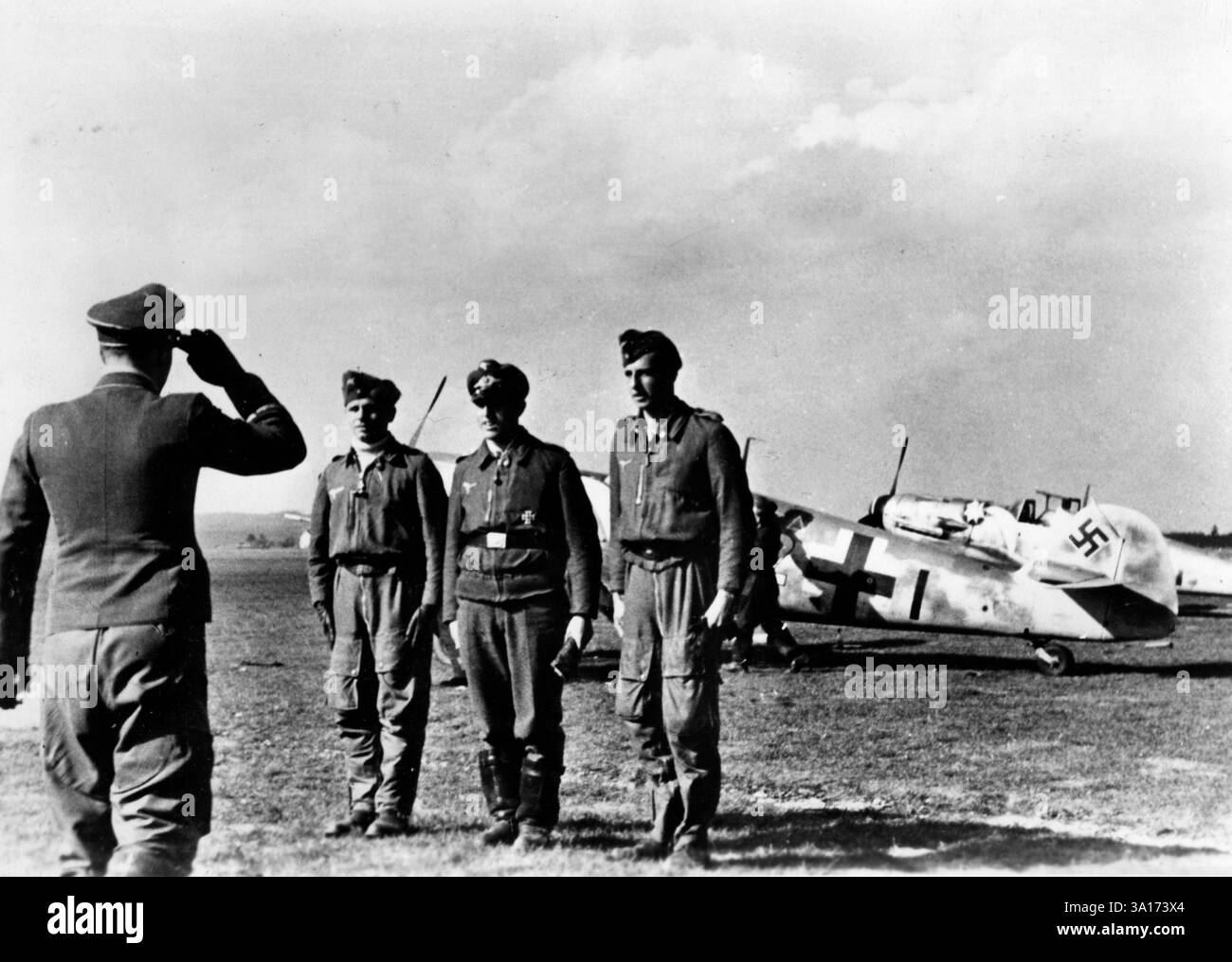 Ein Commodore grüßt drei Piloten, die während des Fluges einen Feind erschossen haben. Messerschmitt mir 109 Kampfflugzeuge im Hintergrund. [Automatisierte Übersetzung] Stockfoto