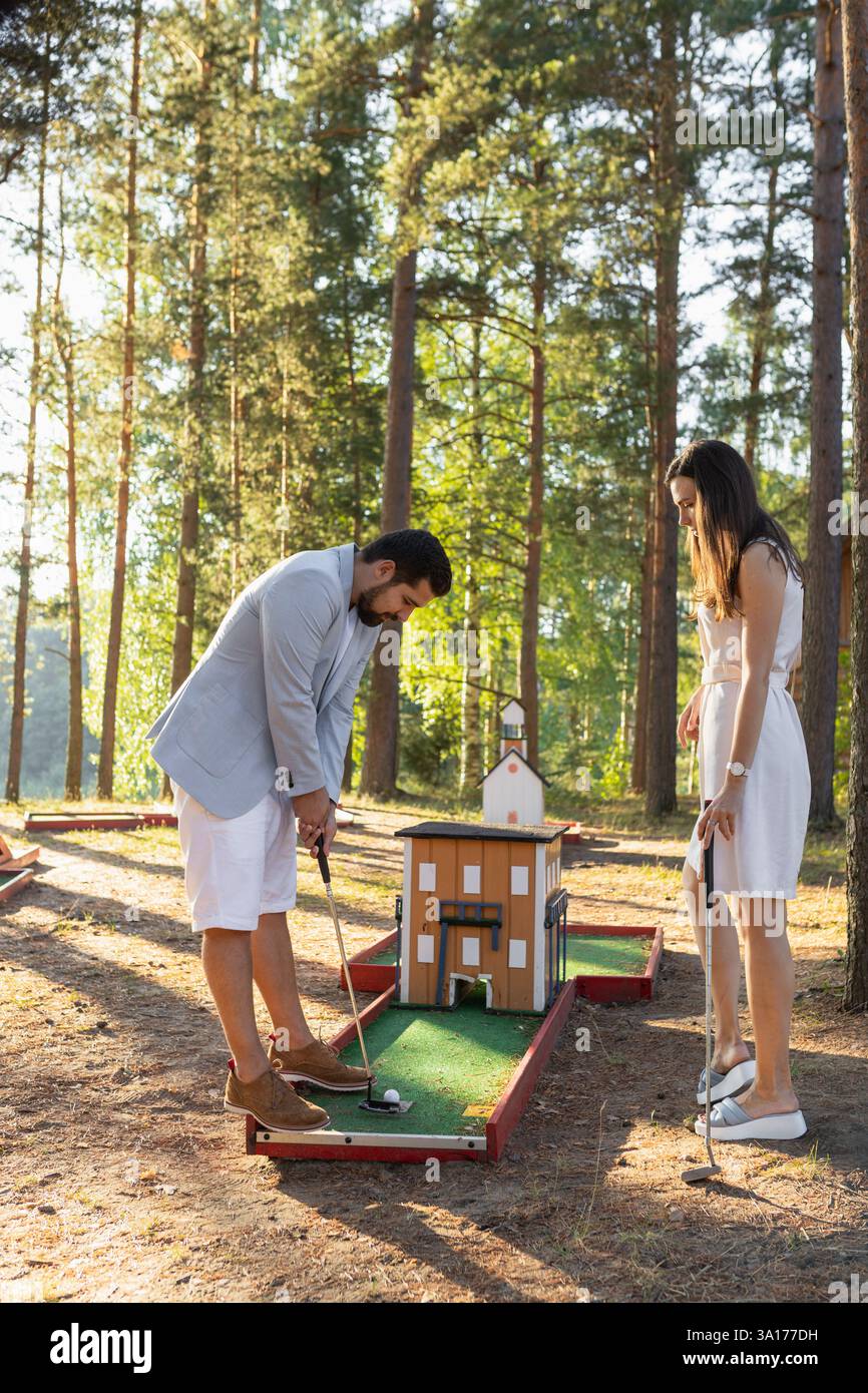 Junges erwachsenes Paar, das Minigolf auf dem Außenplatz im Wald spielt Stockfoto