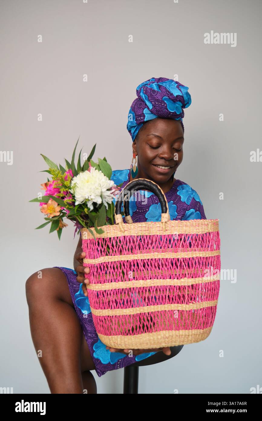 Lächelnde schwarze Frau mit Blumen und rosa gewebter Tasche Stockfoto
