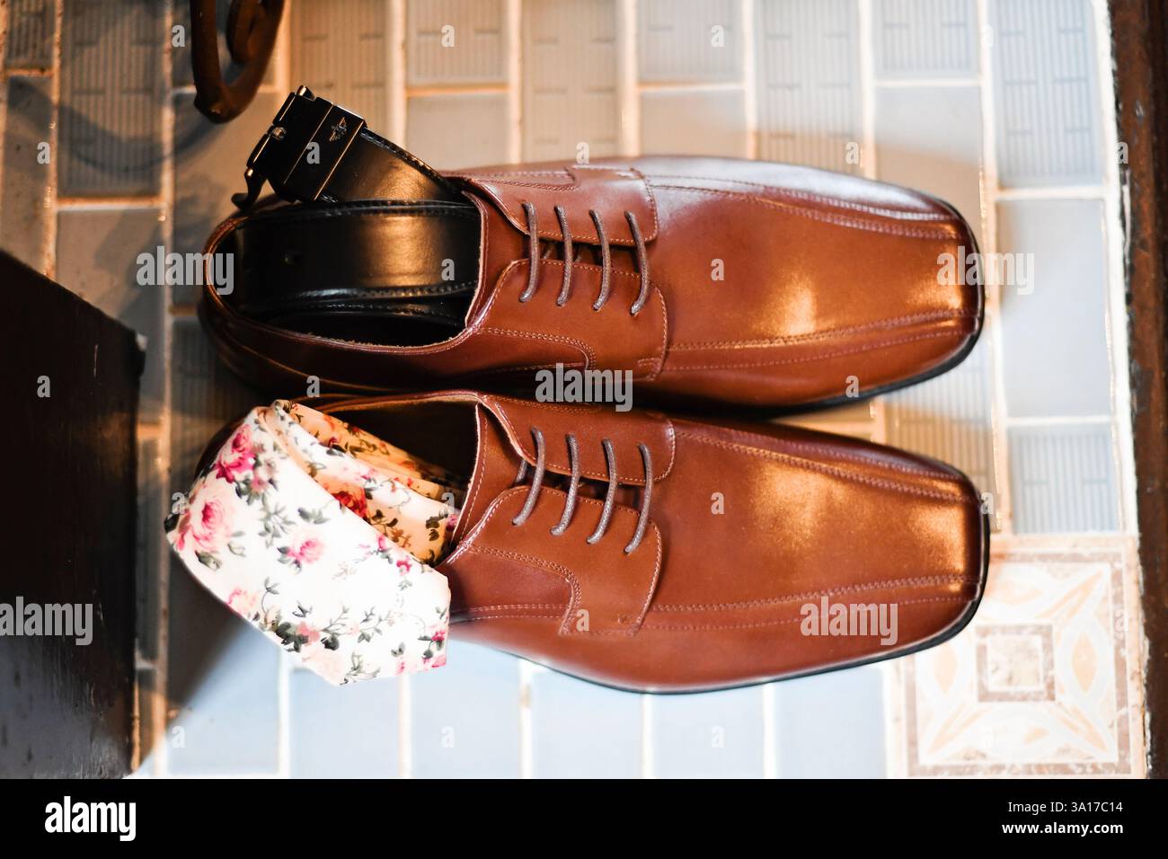 Braune Lederschuhe mit Blumensocken und schwarzem Gürtel. Stockfoto