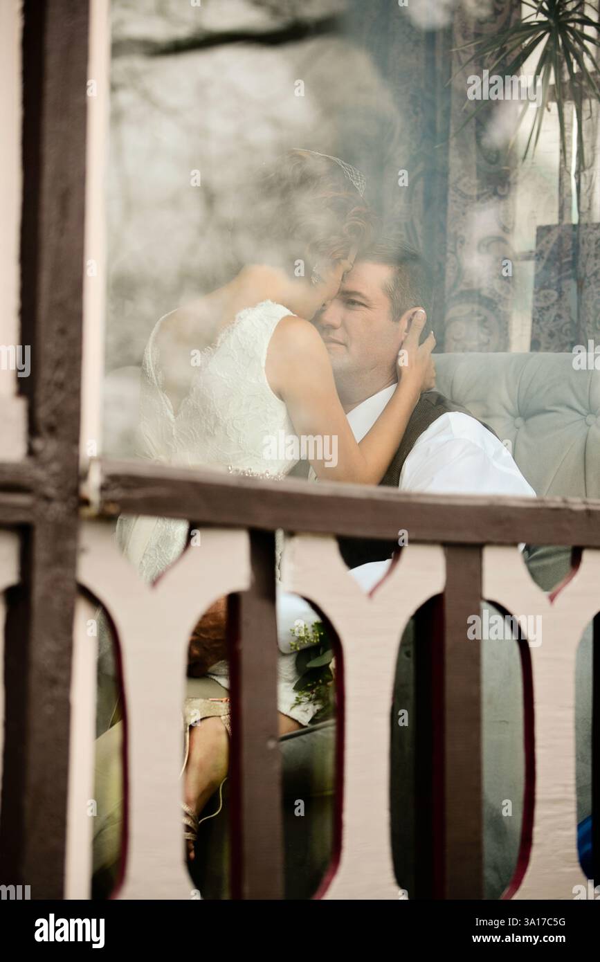 Braut und Bräutigam teilen einen intimen Moment durch einen Fensterreflex Stockfoto