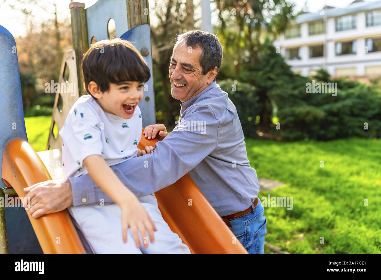 Großvater und Enkel genießen einen sonnigen Tag im Park, spielen auf der Rutsche und lachen zusammen Stockfoto
