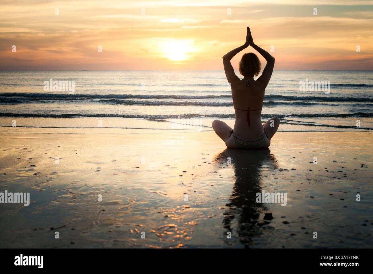 Die Silhouette einer Frau, die während eines ruhigen Sonnenuntergangs am Wasser meditiert und Frieden und Ruhe ausstrahlt. Stockfoto