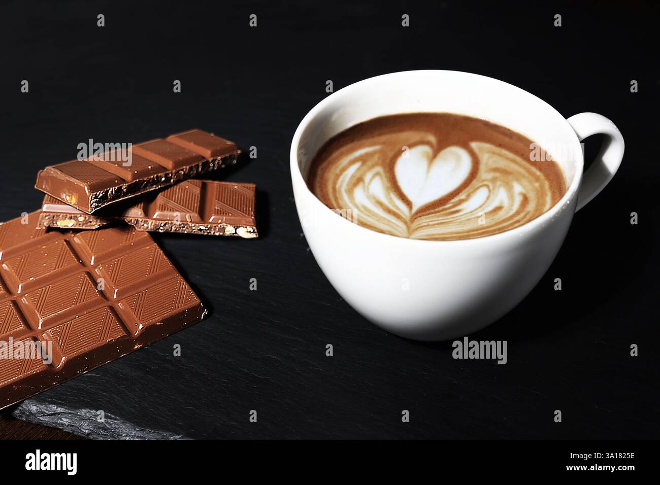 Eine Tasse Cappuccino mit einer Tafel Milchschokolade. Herz auf Cappuccino-Schaum. Barista Stockfoto