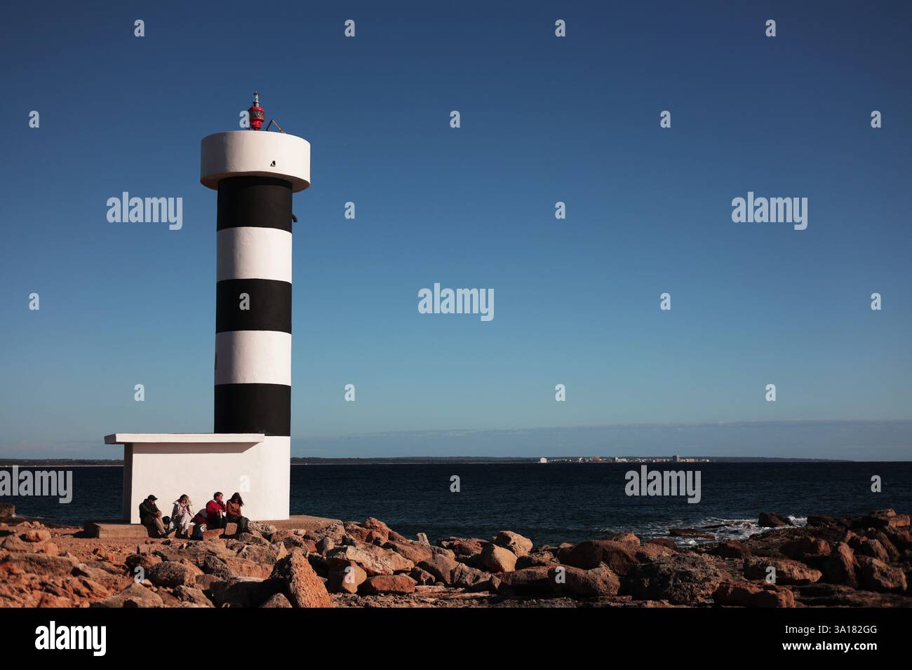 Touristen sitzen in der Nähe des Leuchtturms an der Küste. Familie zusammen, die in der Nähe des Leuchtturms am Meer mit Blick auf die W Stockfoto