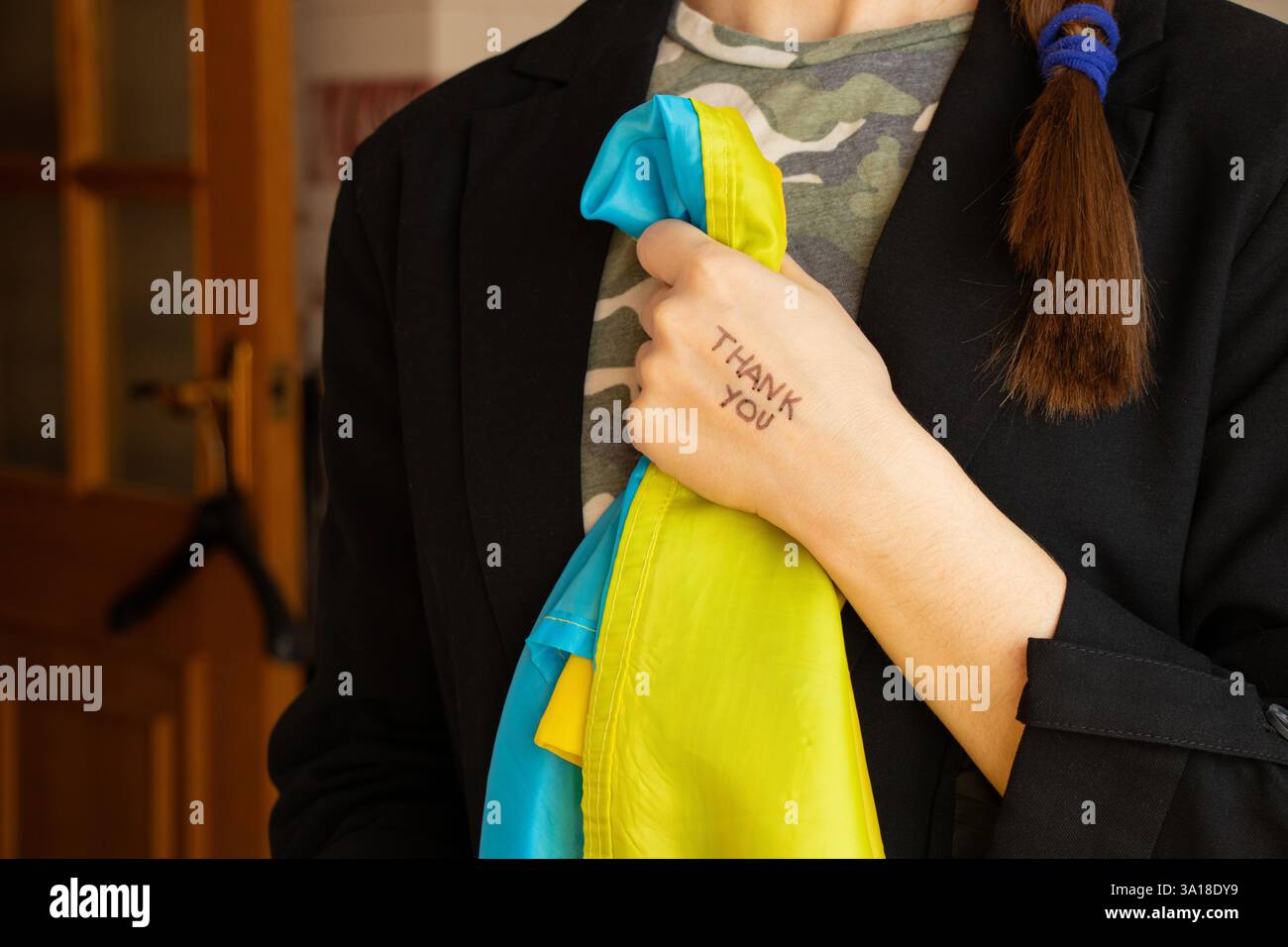 Danke steht auf der Hand eines Mädchens, das eine ukrainische Flagge hält und eine schwarze Geschäftsjacke und ein Camouflage-T-Shirt trägt. Danke Stockfoto
