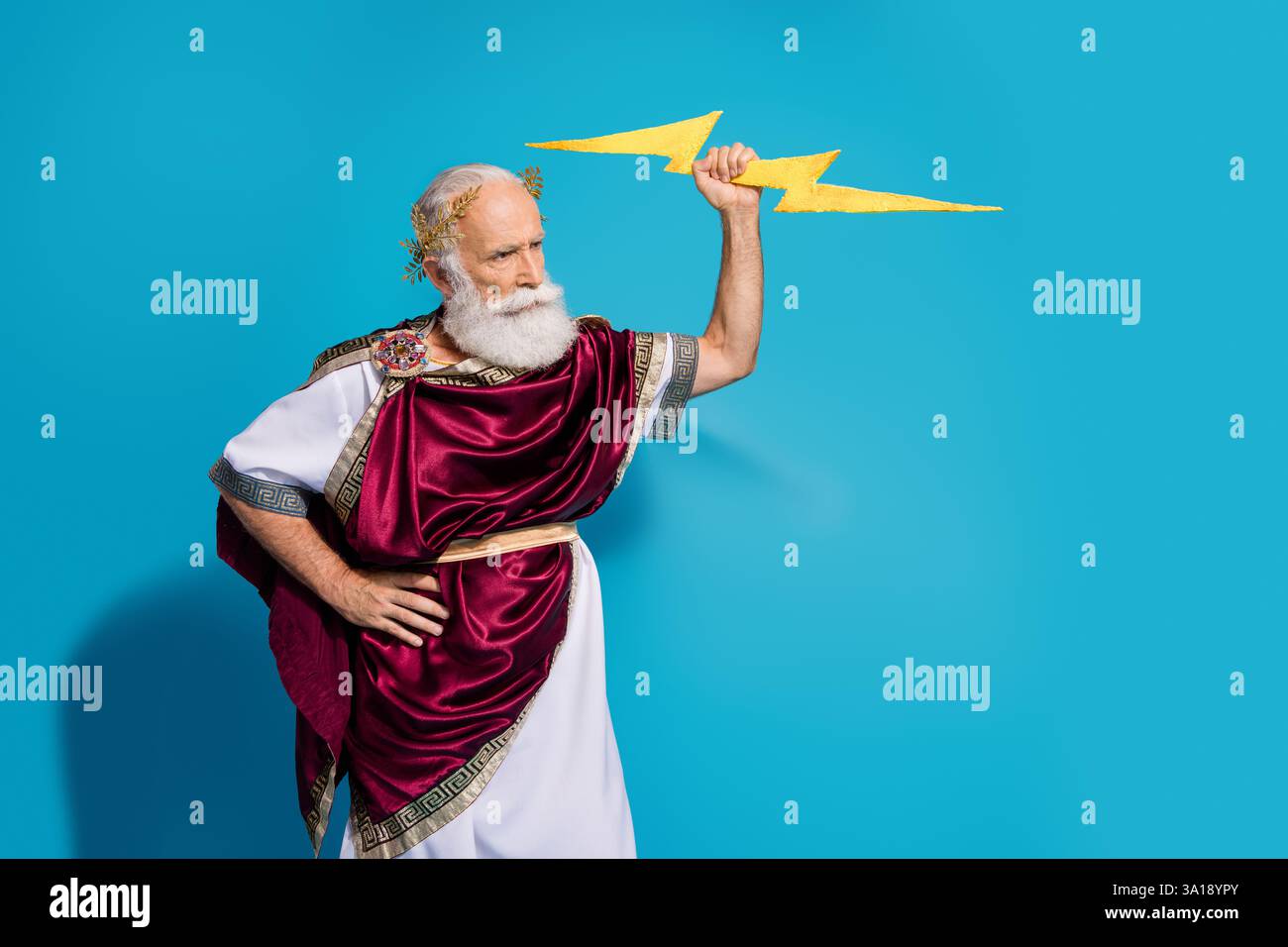 Foto von gutaussehenden älteren männlichen Hit Blitzwetter Tragen alten griechischen Gott König Kleid isoliert auf blauem Hintergrund Stockfoto