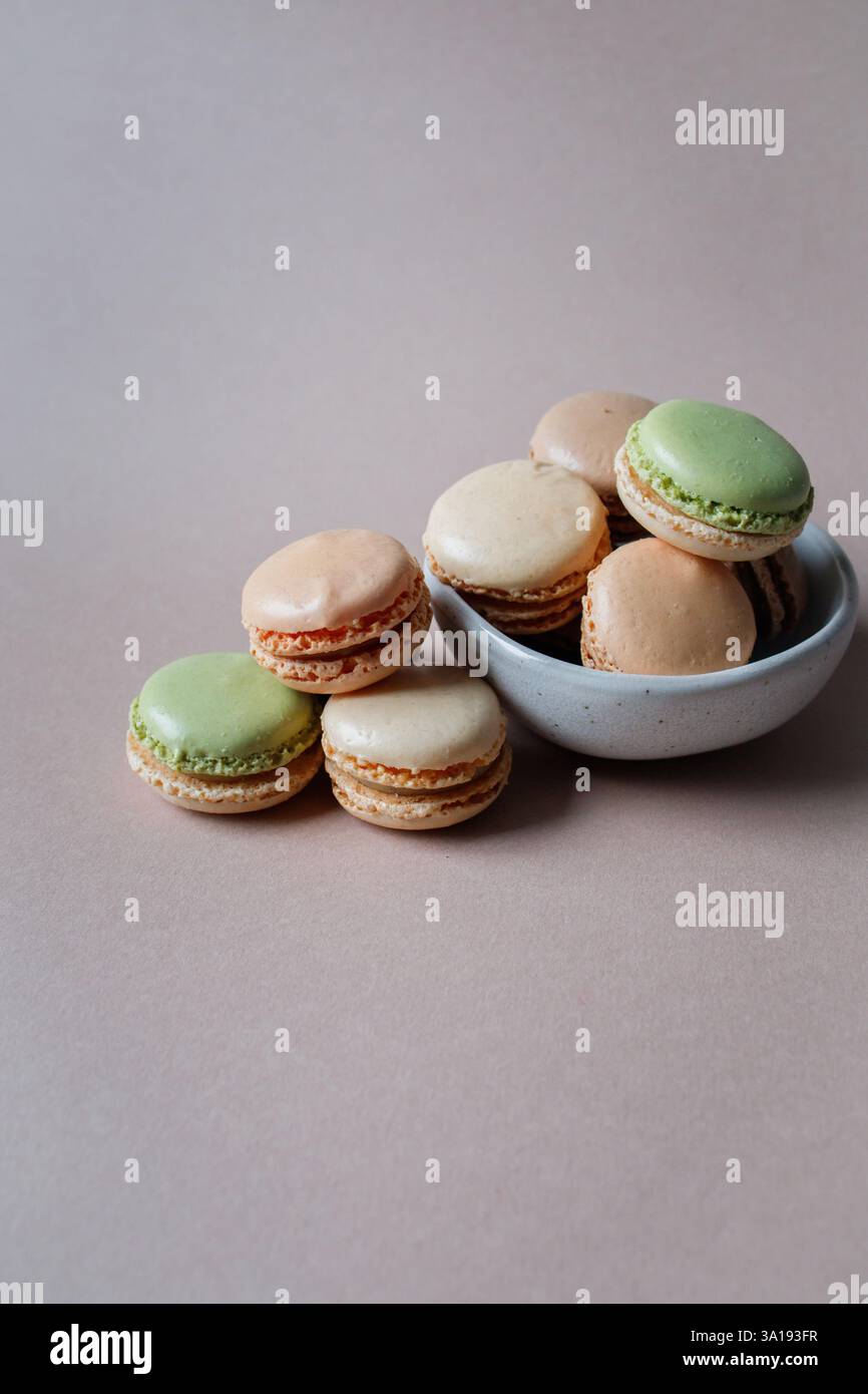 Französische, mehrfarbige Mini-Macarons in einer kleinen Schüssel auf beigem Hintergrund Stockfoto
