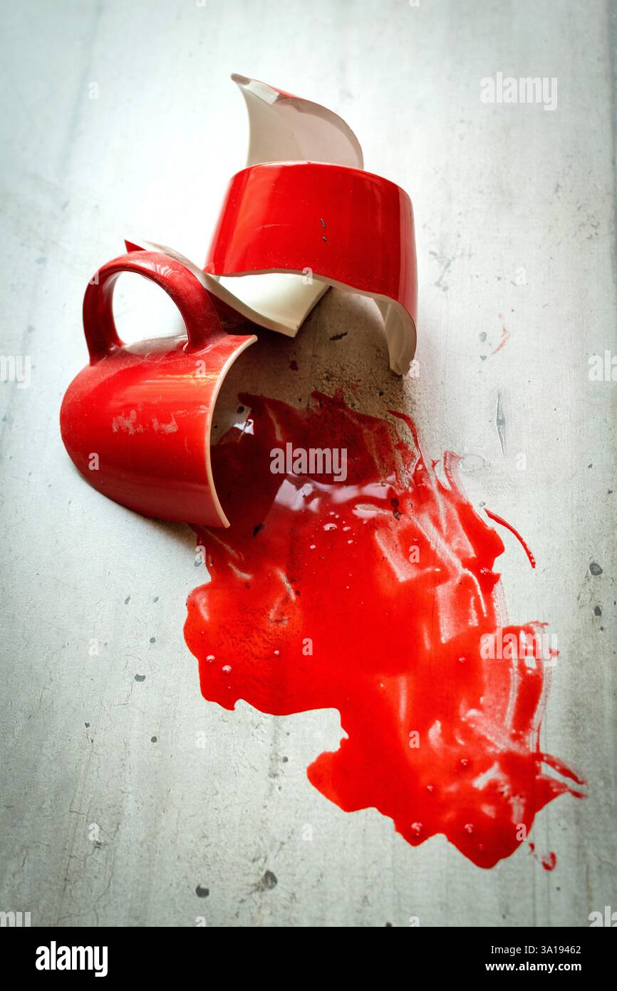 Ein roter Keramikbecher liegt auf einer hellen Oberfläche zerbrochen, aus der leuchtend rote Flüssigkeit austritt. Stockfoto