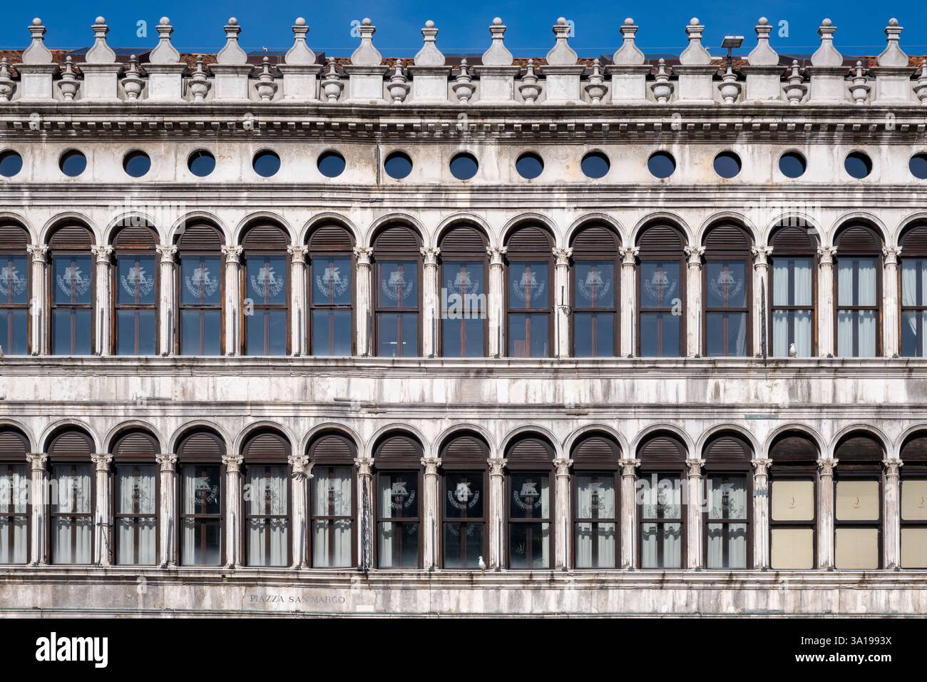 Die kunstvolle Fassade eines historischen Gebäudes auf der Piazza San Marco mit klassischen Bogenfenstern und komplexen architektonischen Details. Stockfoto