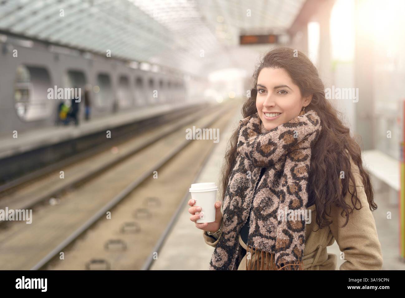 Lächelnde Frau in hellen Braun Winter Mantel und Kaffee Tasse in der hand im stehen am s-Bahn-Bahnsteig Einzel Stockfoto