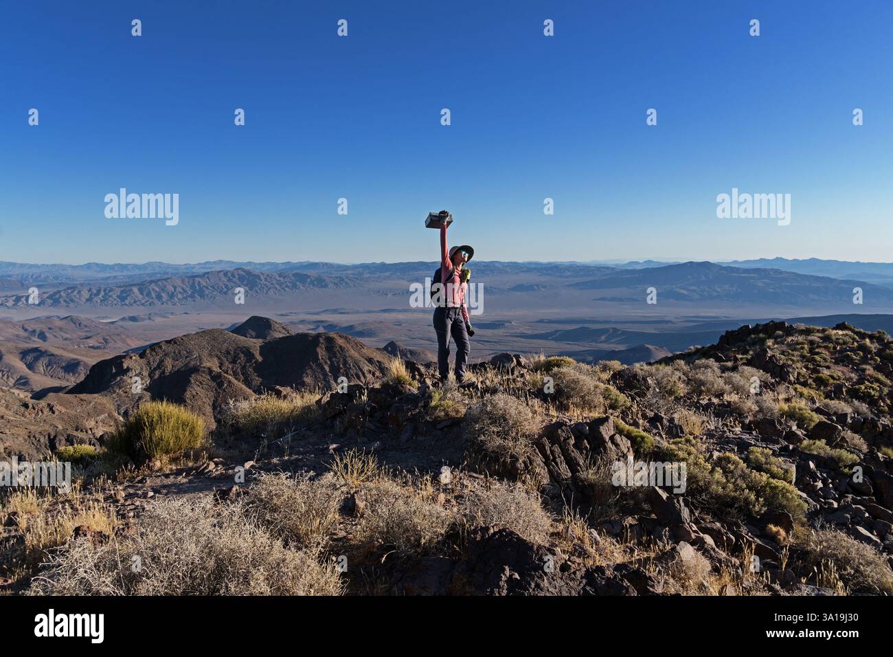 Frau auf dem Needle Peak im Death Valley National Park, die das Gipfelregister über dem Kopf hält, als Triumph mit blauem Himmel Copyspace Stockfoto