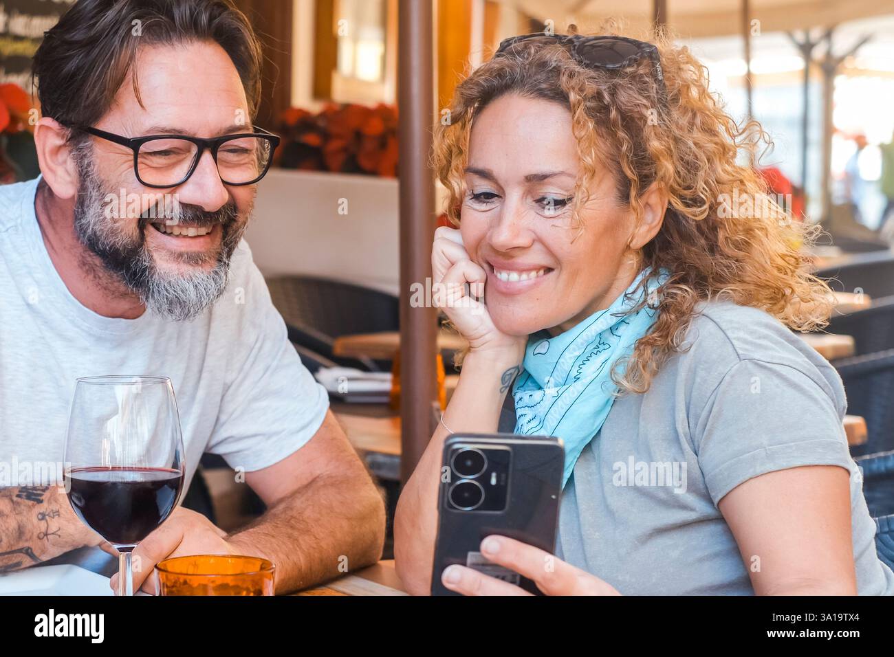 Weißes Paar liest Telefonbenachrichtigungen vor dem Mittagessen und sitzt zusammen am Restauranttisch und hat Spaß. Leute, die sich Kommentare ansehen oder online wählen, was sie essen möchten Stockfoto