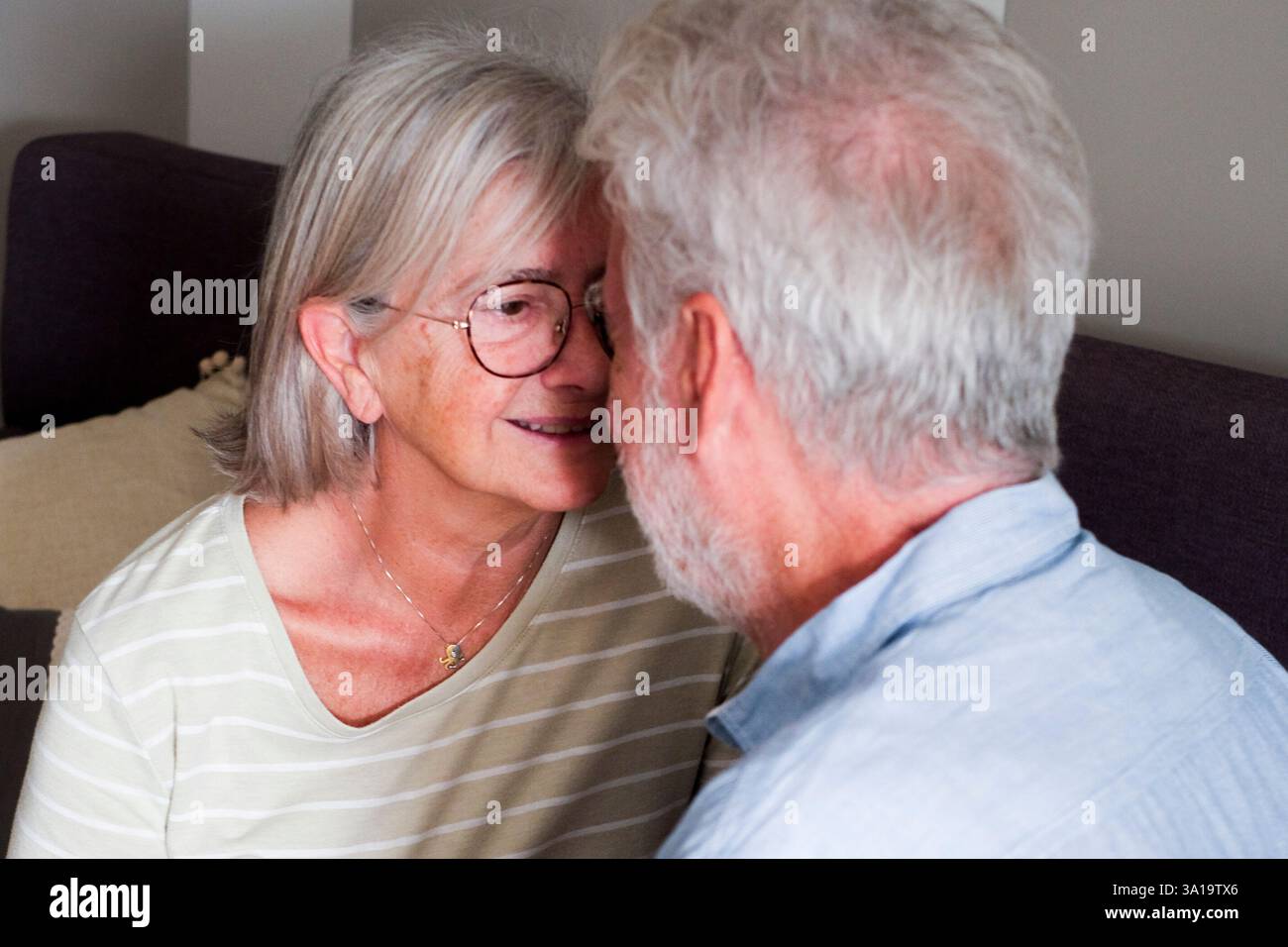 Herzerwärmende Szene eines reifen Paares, eines liebevollen Mannes und einer liebevollen Frau, die zu Hause auf dem Sofa kuschelt. Die Großeltern teilen süße Momente der Zuneigung, flirten und plaudern gemütlich drinnen und genießen ihre goldenen Jahre miteinander Stockfoto
