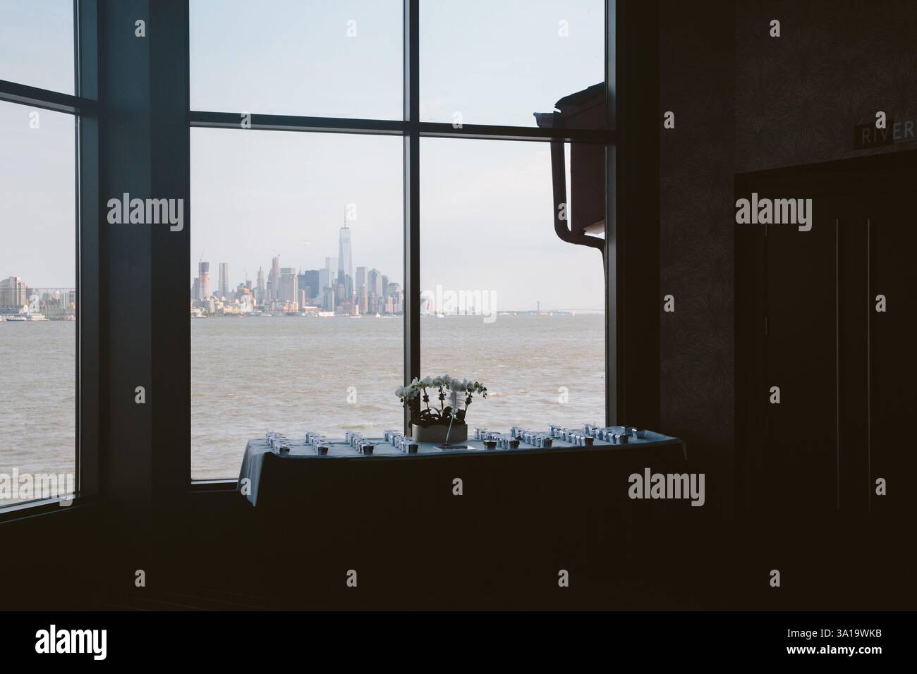 Eine schöne Indoor-Szene mit einem Blumentisch und einem atemberaubenden Blick auf die Skyline von New York City am Wasser. Stockfoto Eine schöne Indoor-Szene mit einem Blumentisch und einem atemberaubenden Blick auf die Skyline von New York City am Wasser. Stockfoto