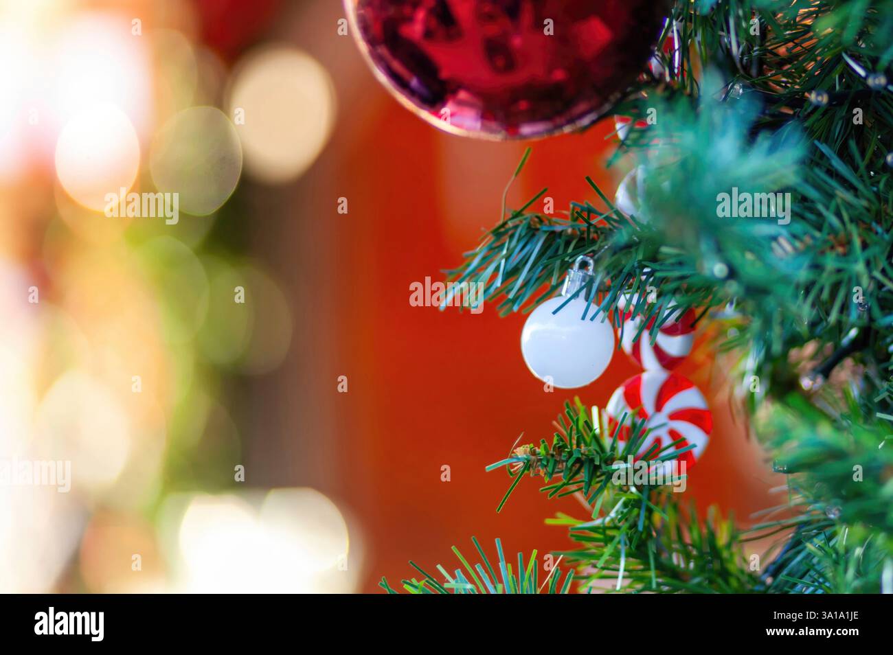 Weihnachtsbaumzweige mit bunten Ornamenten und Zuckerstangen, die einen warmen und festlichen Weihnachtsgeist mit einem verschwommenen Hintergrund wecken Stockfoto