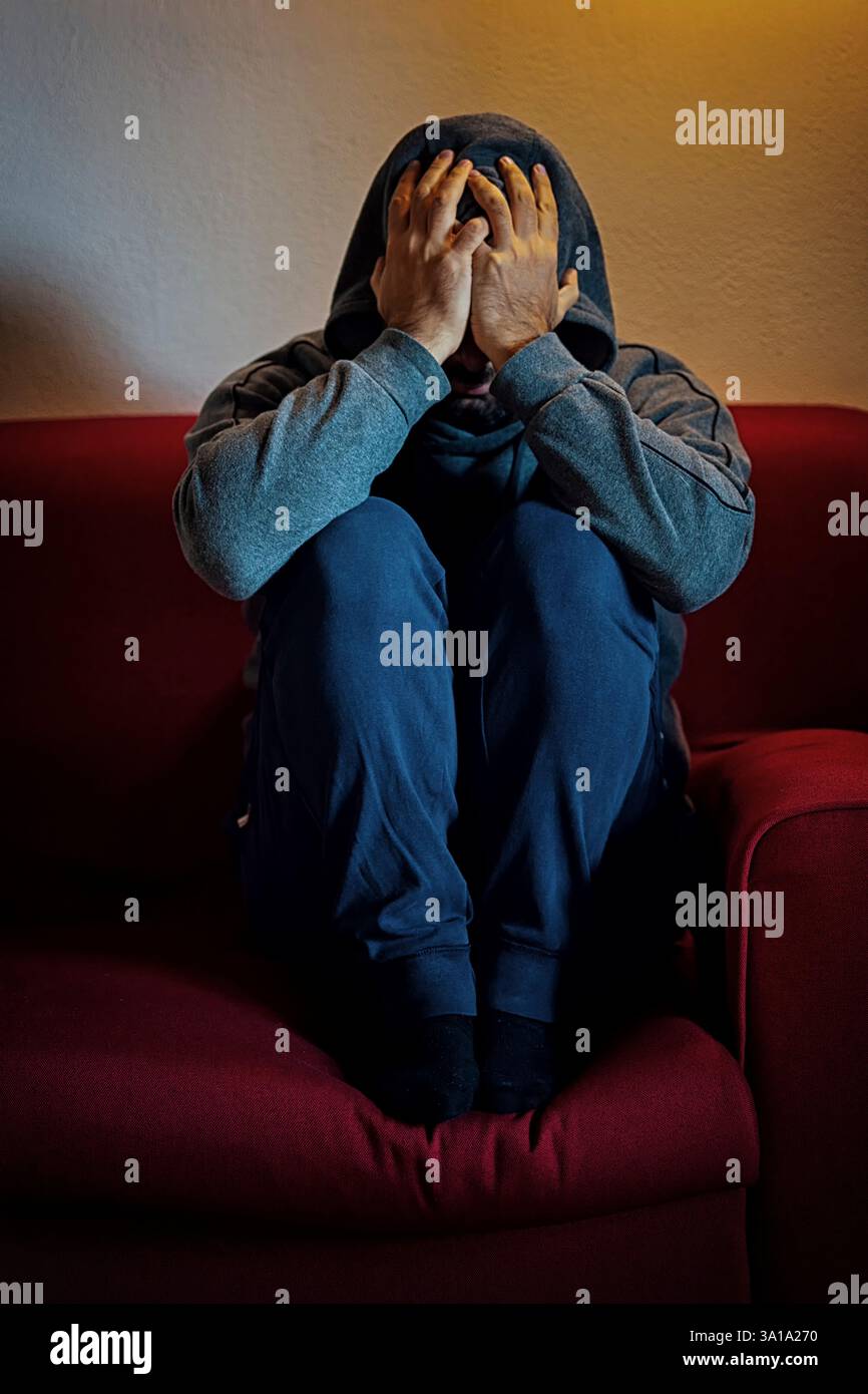 Der Mann sitzt auf einer Couch, überwältigt von Depressionen und Einsamkeit, reflektiert psychische Gesundheitsprobleme Stockfoto