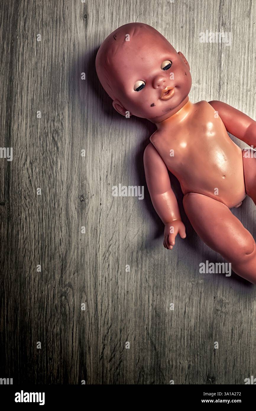 Eine gruselige Vintage-Puppe liegt auf einem grauen Holzboden und erinnert an Nostalgie und Einsamkeit in einer eindringlichen Atmosphäre Stockfoto