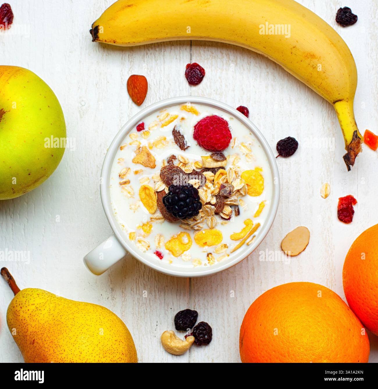 Frühstück mit einer Schüssel Milch, Müsli und rotem Obst auf einem weißen Tisch und frischem Obst. Stockfoto