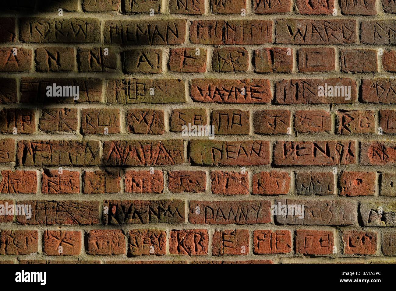 Eine Backsteinmauer im Dorf Romsey Hampshire England, bedeckt mit Graffiti-Namen, die in den Backstein gehauen sind. Stockfoto