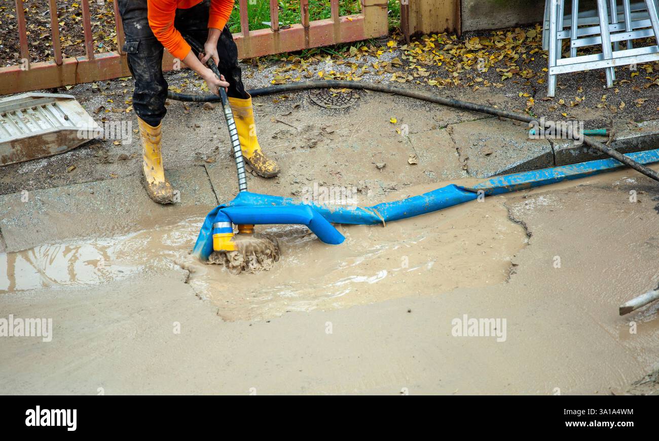 Ein Arbeiter repariert eine kaputte Wasserleitung auf der Straße, indem er eine Pumpe benutzt, um den Graben zu leeren. Stockfoto